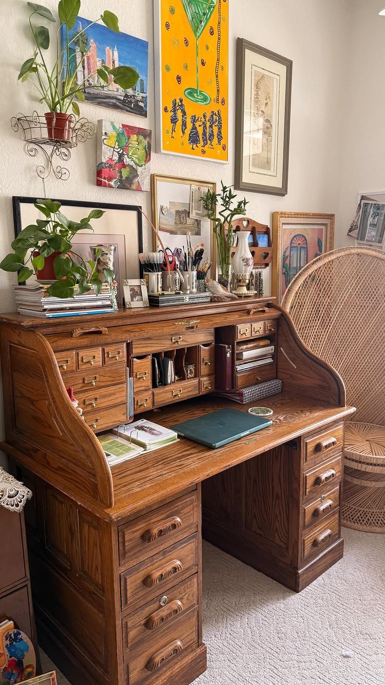 Wooden roll-top desk with a green leather top and various art on the wall