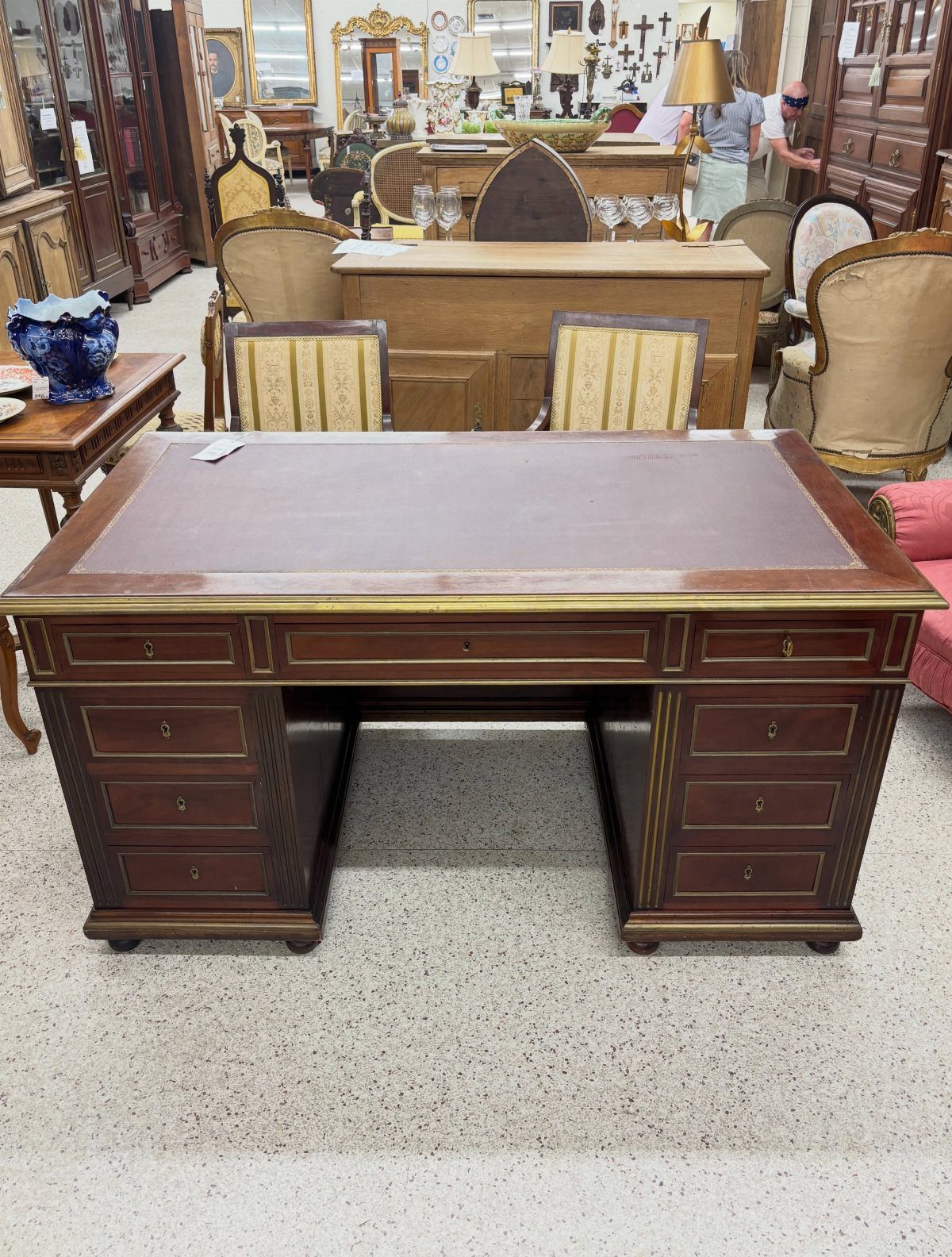 Antique wooden desk with a brown leather top and gold trim in a store