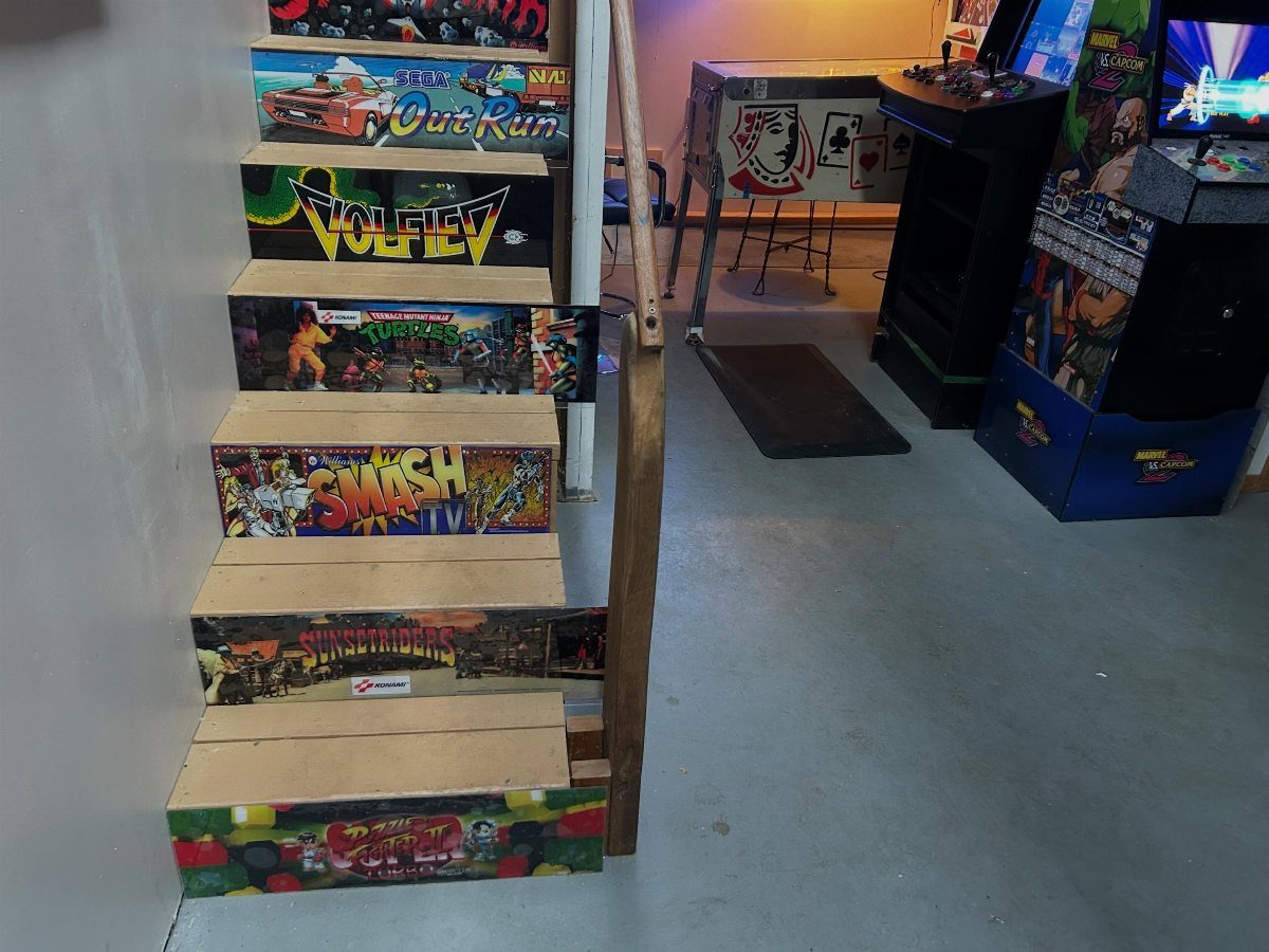 Wooden stairs with arcade game graphics leading into a game room with cabinets.