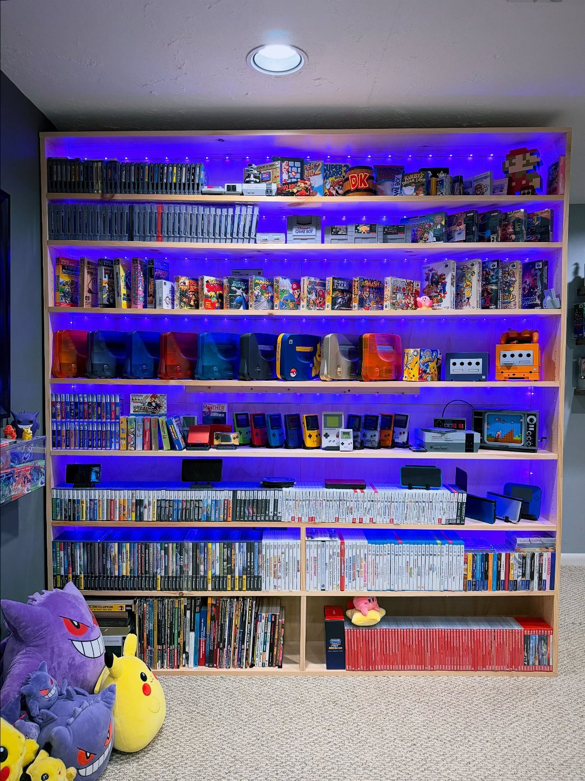 Wooden shelves filled with video games and collectibles lit by purple LED strips.