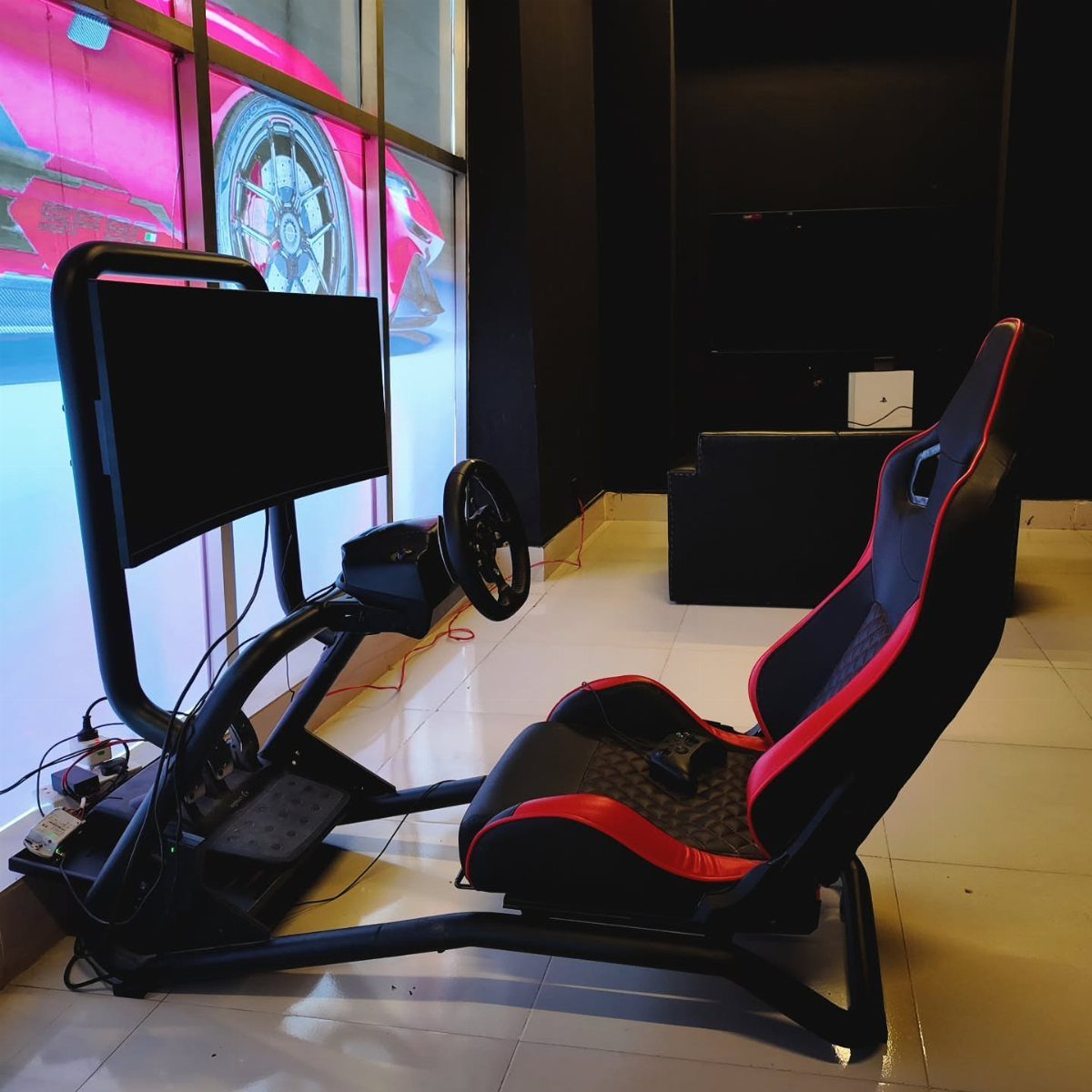 Racing simulator setup with red and black seat, steering wheel, and monitor.