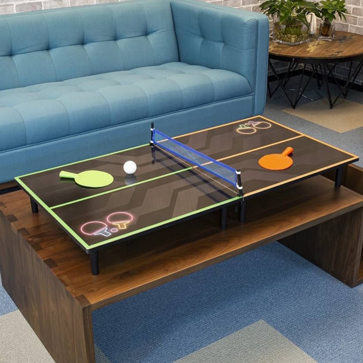 Miniature designer ping pong table with neon accents on a wooden coffee table.