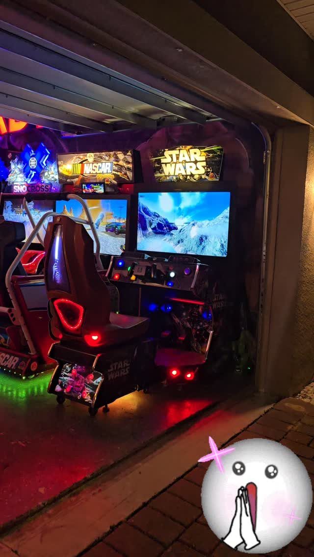 Home arcade game room in a garage with racing seats and multiple screens.