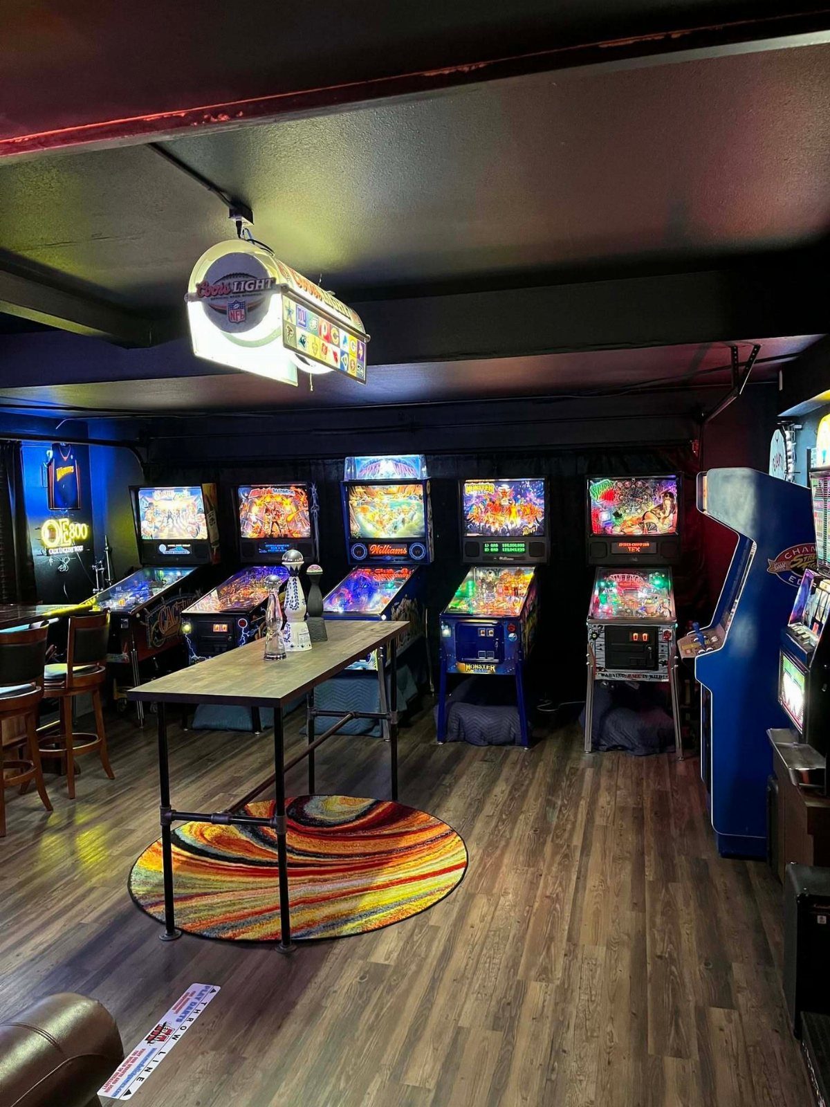 Row of colorful pinball machines and an arcade cabinet in a dark game room