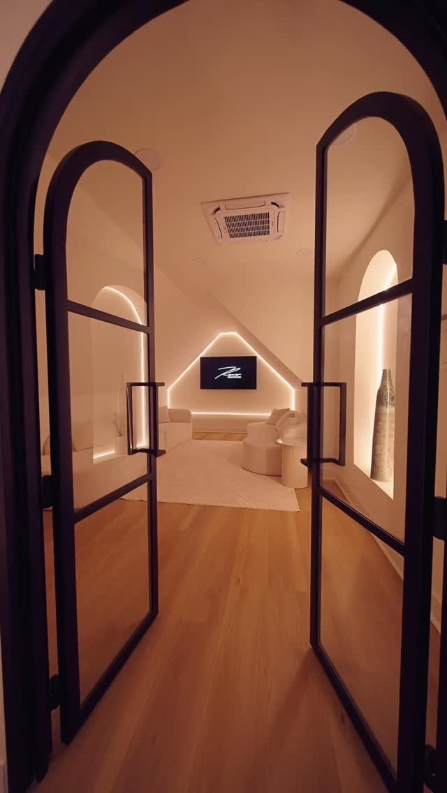 Modern attic room with sloped ceilings seen through open arched glass doors.