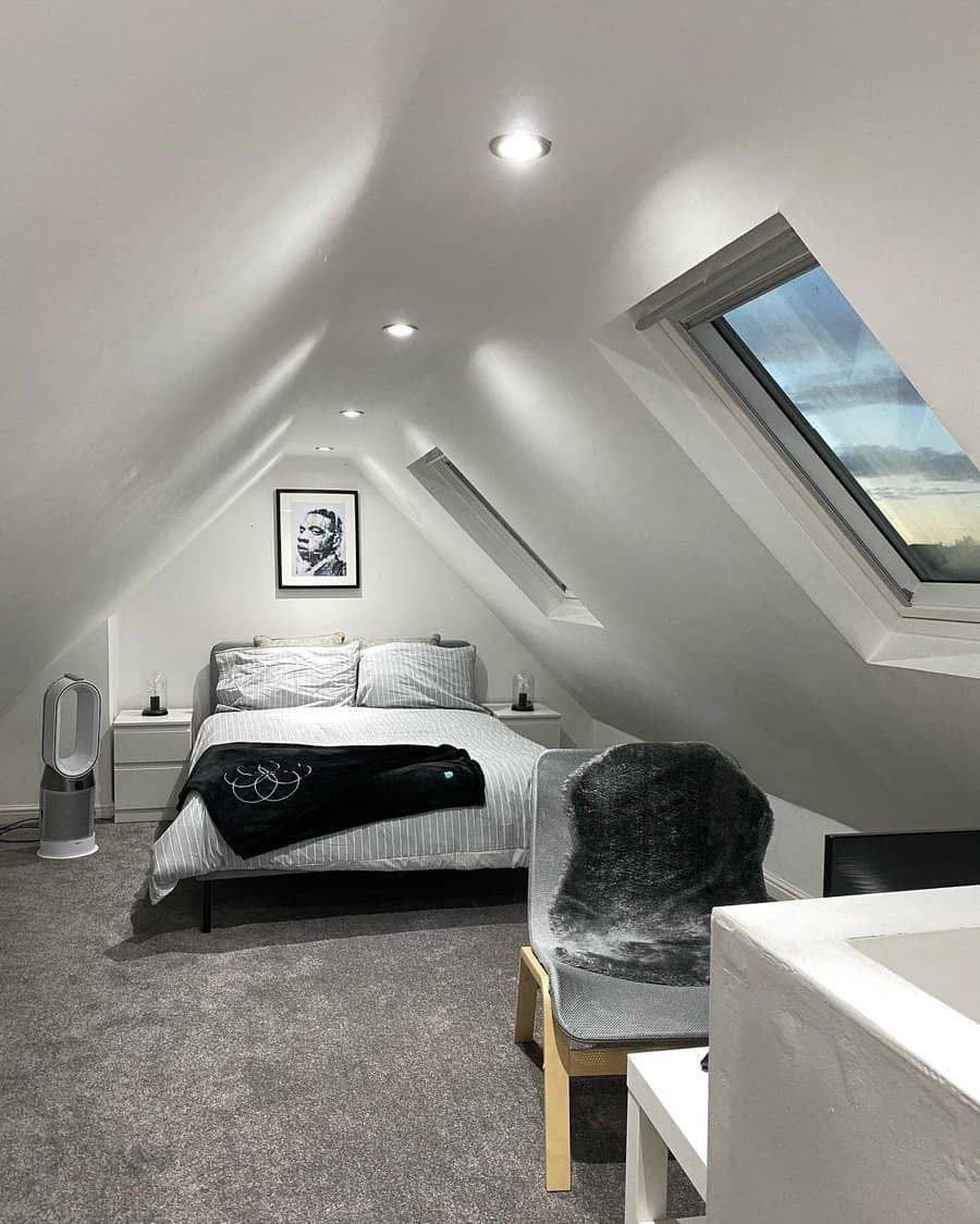 Modern attic bedroom with white sloped ceilings, grey carpet, and two skylights.
