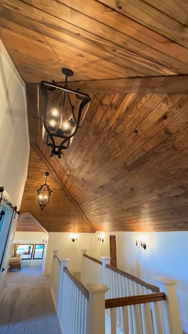 Vaulted wooden ceiling with lantern lights and white railings in a loft hallway.