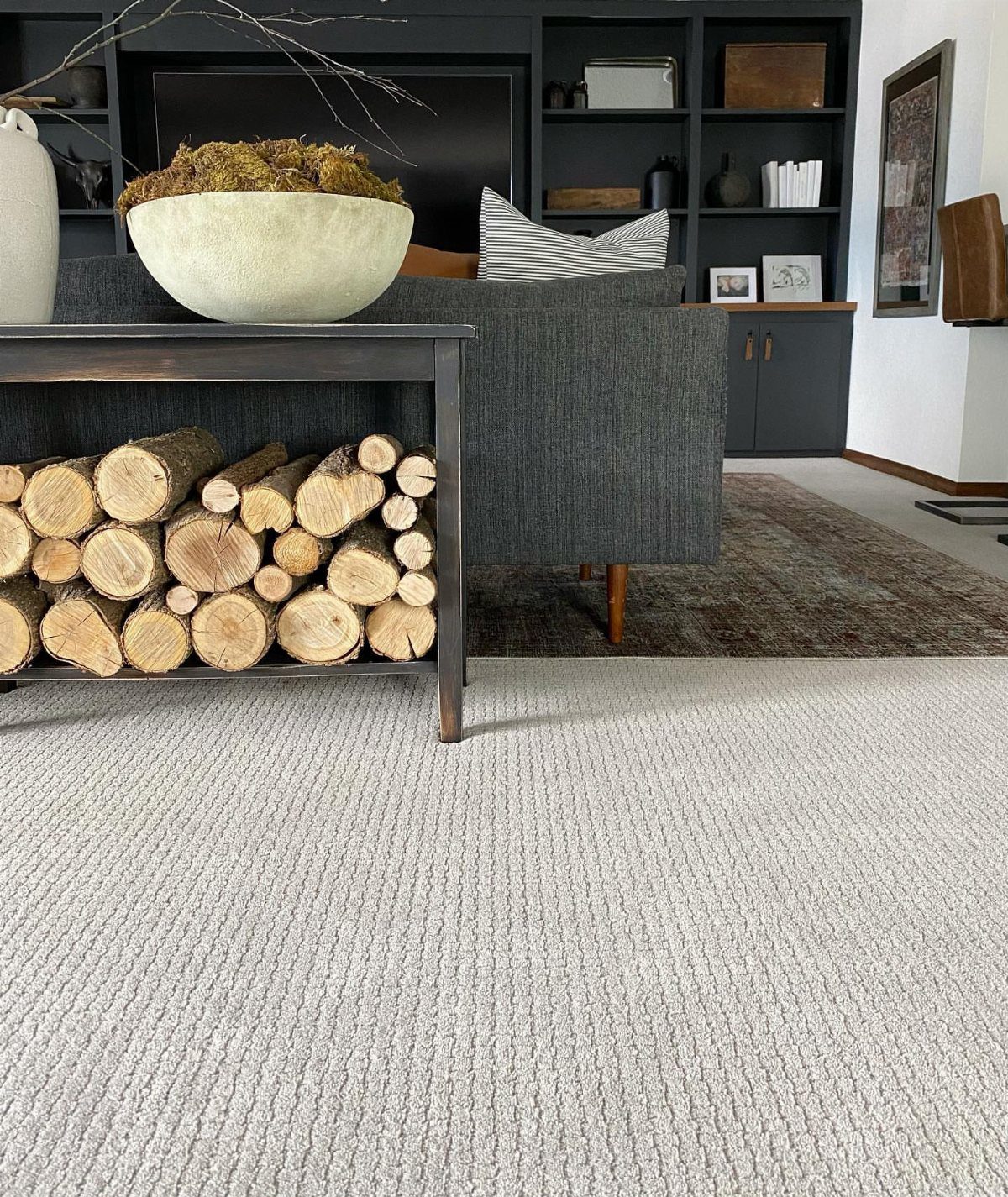 Light grey textured carpet layered over a brown area rug in a living room.