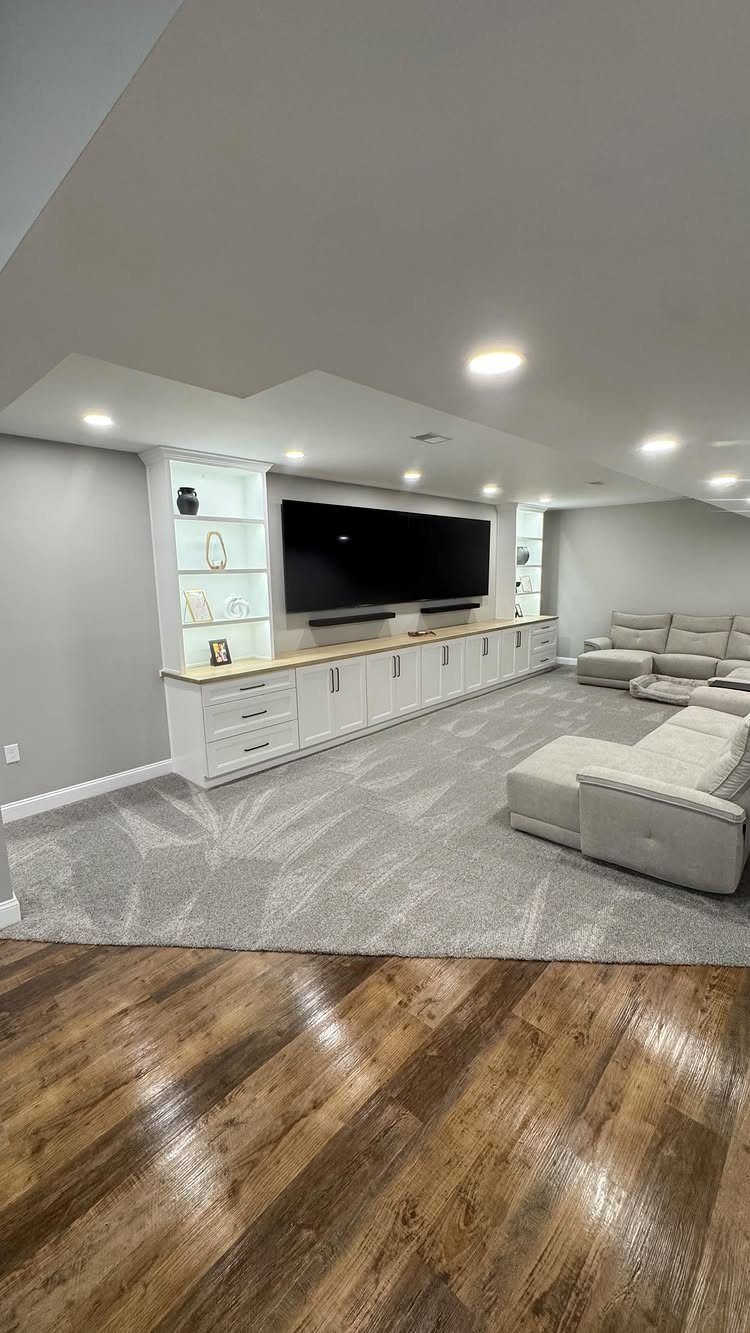 White built-in cabinets and shelves surrounding a large TV in a modern basement.