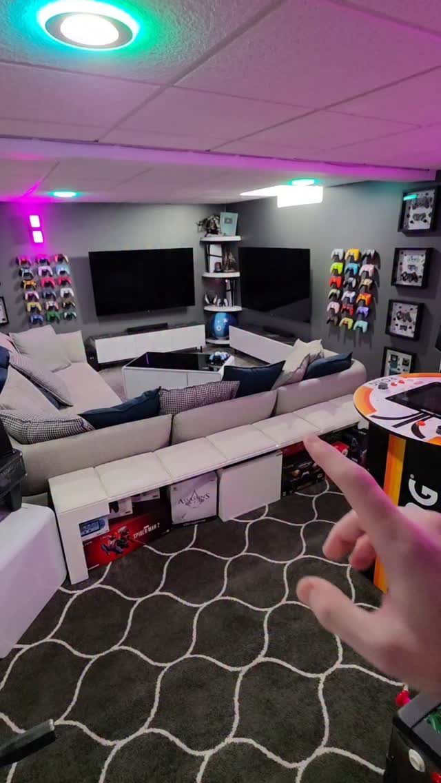 Basement game room with white sectional sofa, dual TVs, and neon accent lighting.