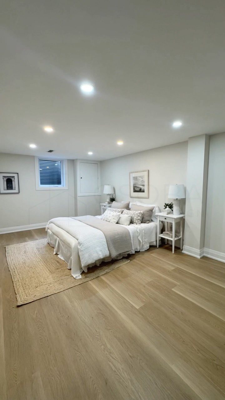 White bed with neutral linens in a bright basement bedroom with wood floors.