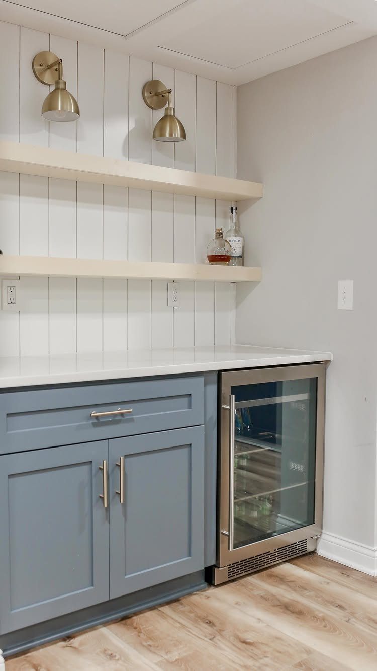Small kitchenette with blue cabinets, white countertops, open shelving, and a beverage refrigerator.