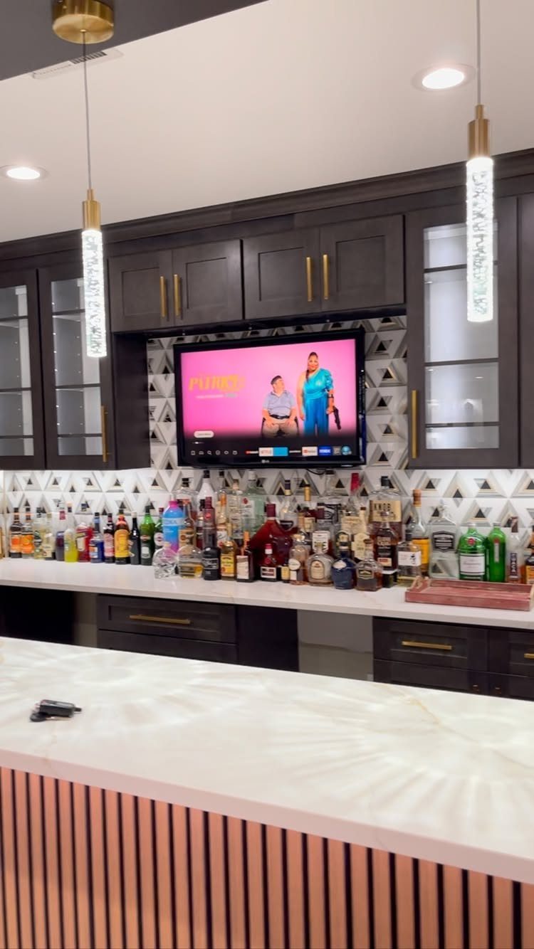 Modern home bar with dark cabinets, liquor bottles, and a white marble island.