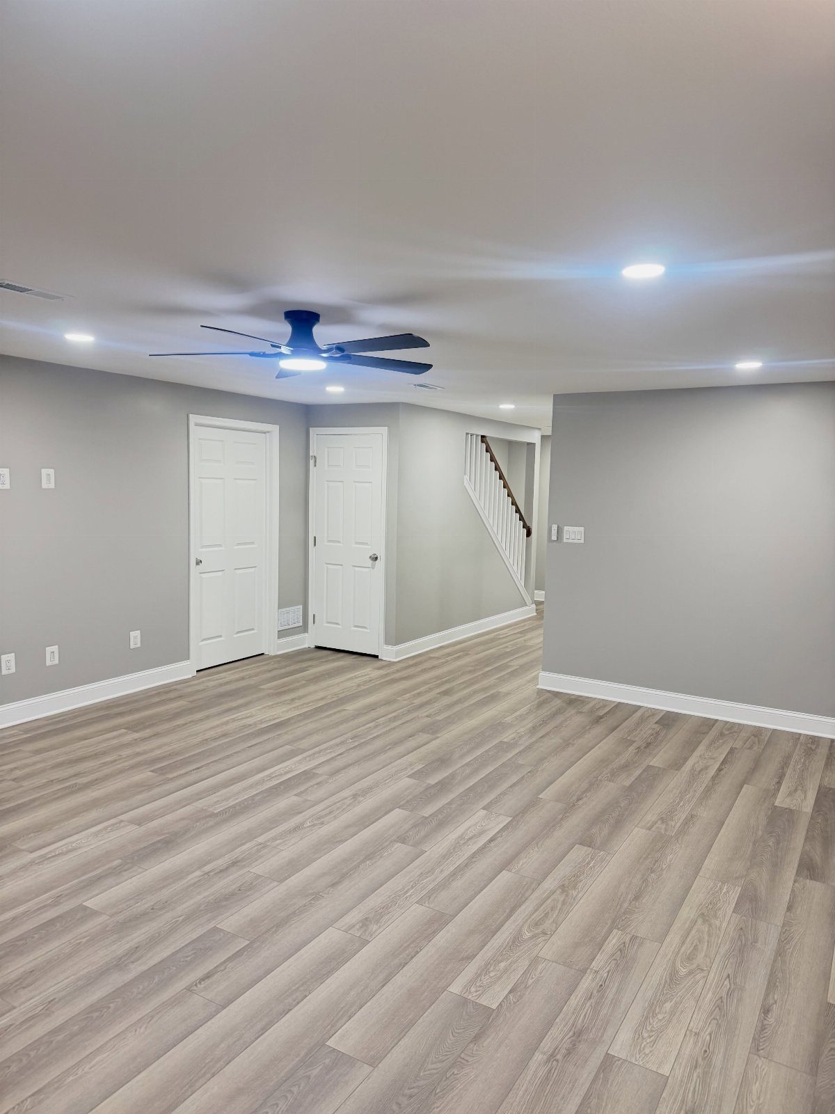 Empty basement room with grey walls, laminate flooring, and recessed ceiling lighting.