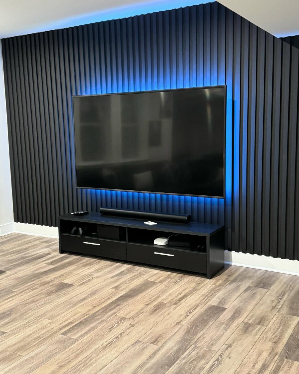 Black vertical wood panel wall with a mounted TV and blue backlight.