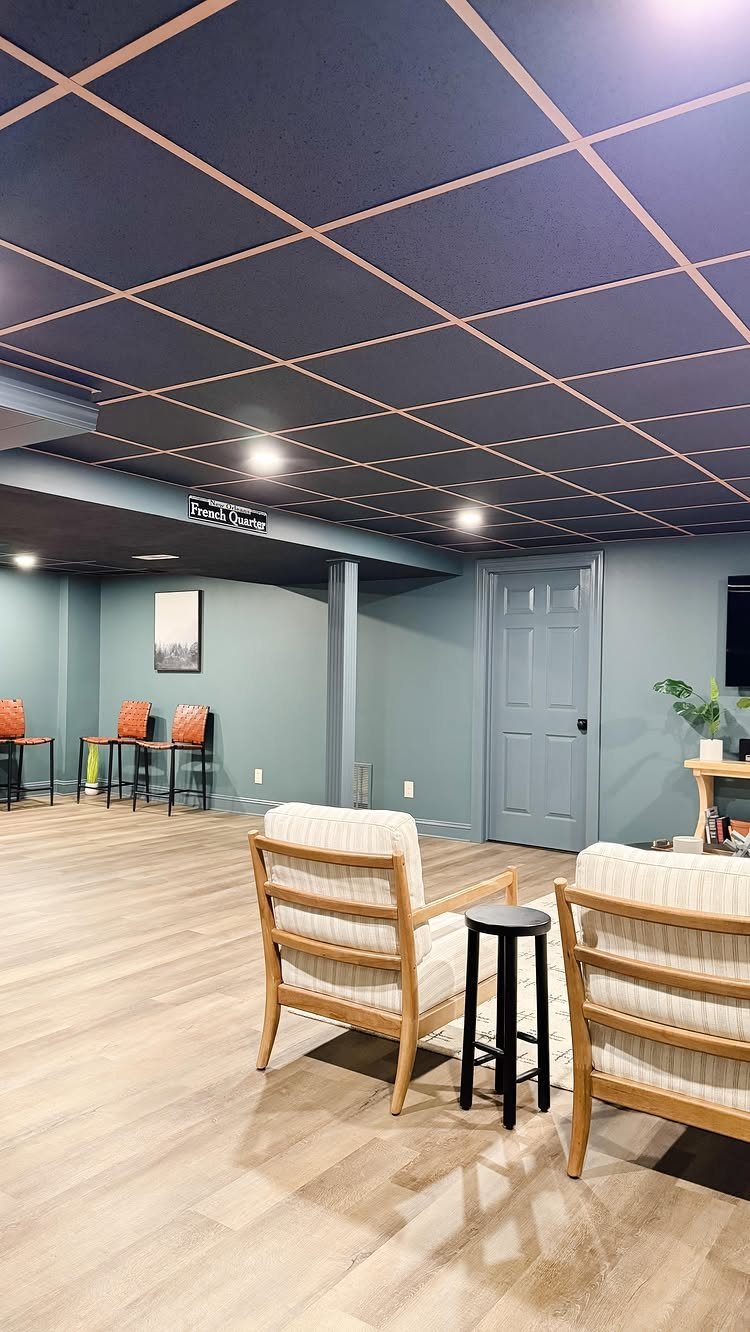 Dark blue grid drop ceiling in a finished basement with modern furniture.