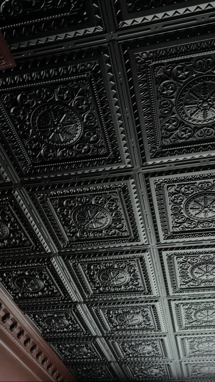 Black embossed ceiling tiles with intricate floral patterns arranged in a grid.