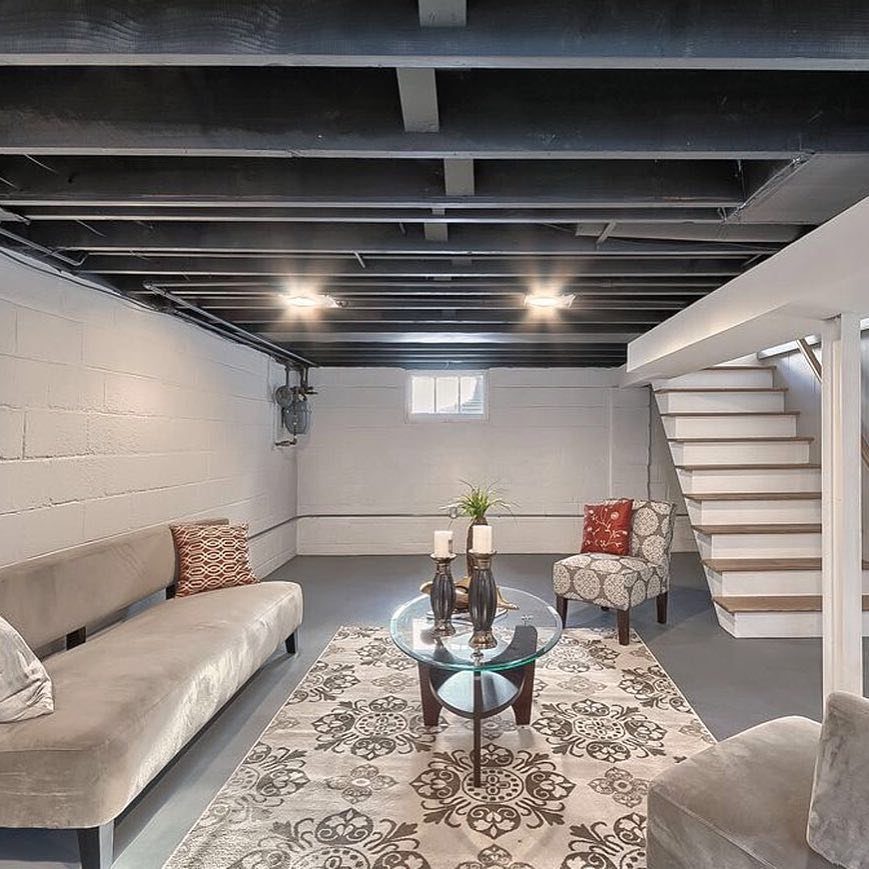 Black painted exposed beams on a basement ceiling above a modern living area.