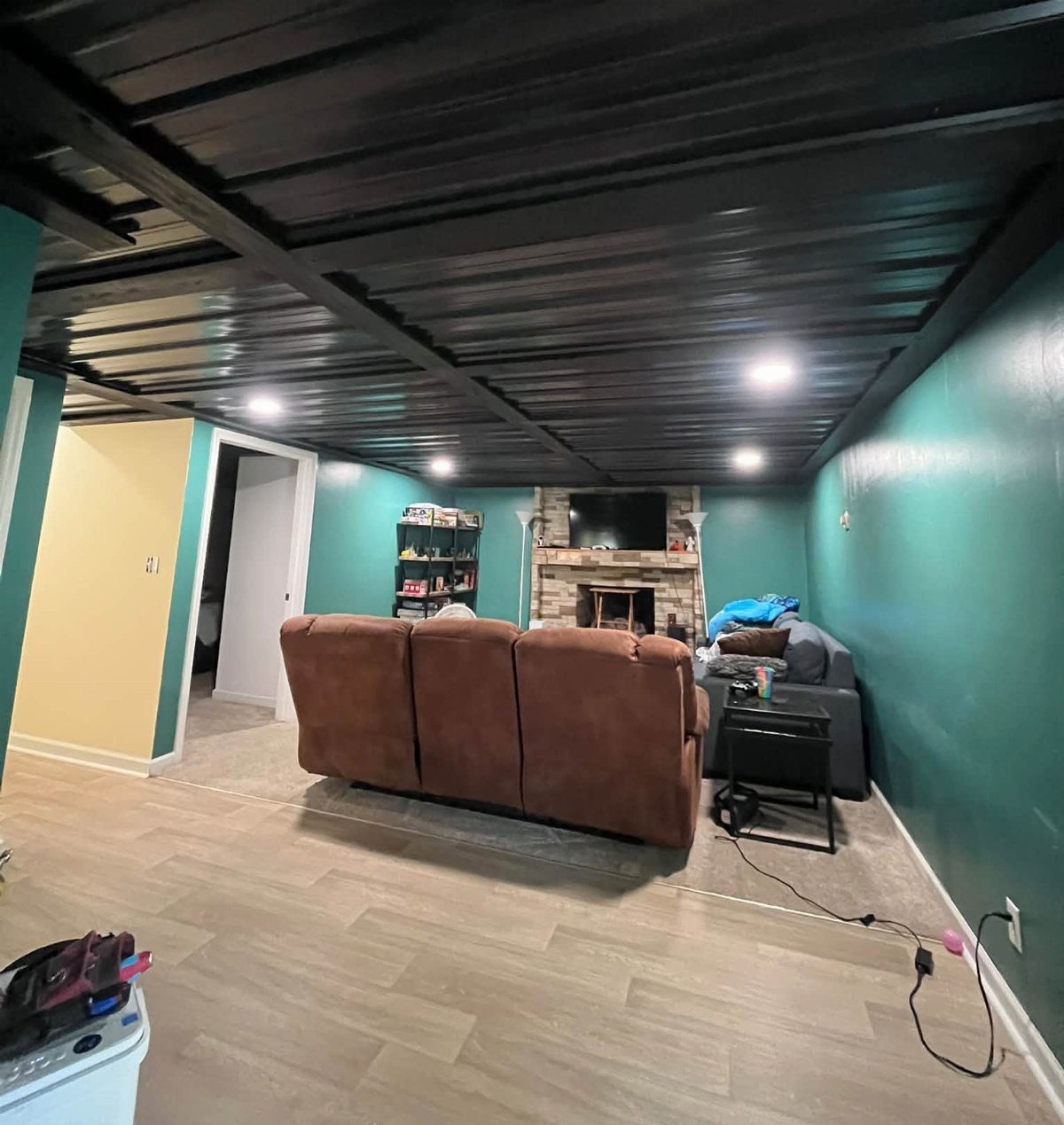 Black painted ceiling with exposed beams in a basement with teal walls