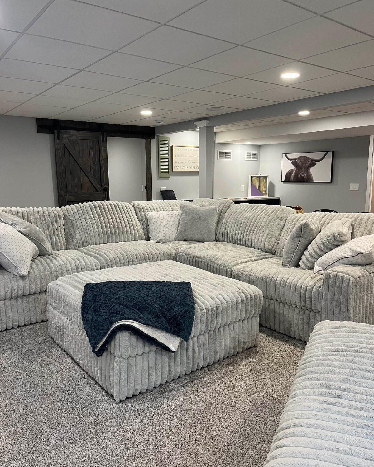 Grey ribbed sectional sofa in a basement with a white drop ceiling
