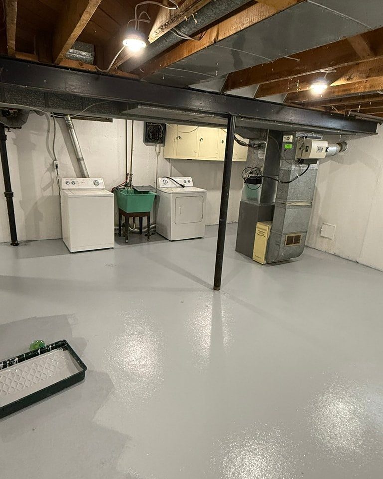 Glossy light gray painted concrete floor in a basement laundry room setting.