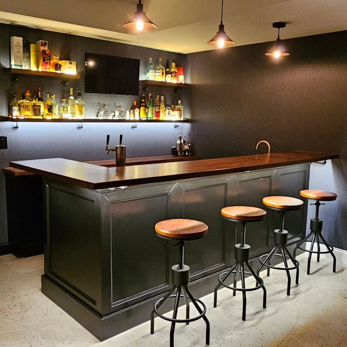 Home bar with dark grey cabinetry, wooden countertop, and industrial bar stools.