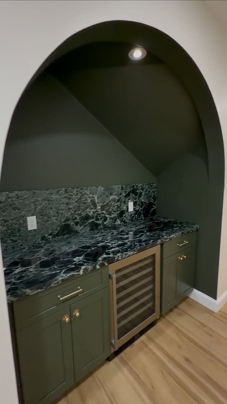 Built-in dry bar with green cabinets and marbled stone in an arched alcove.