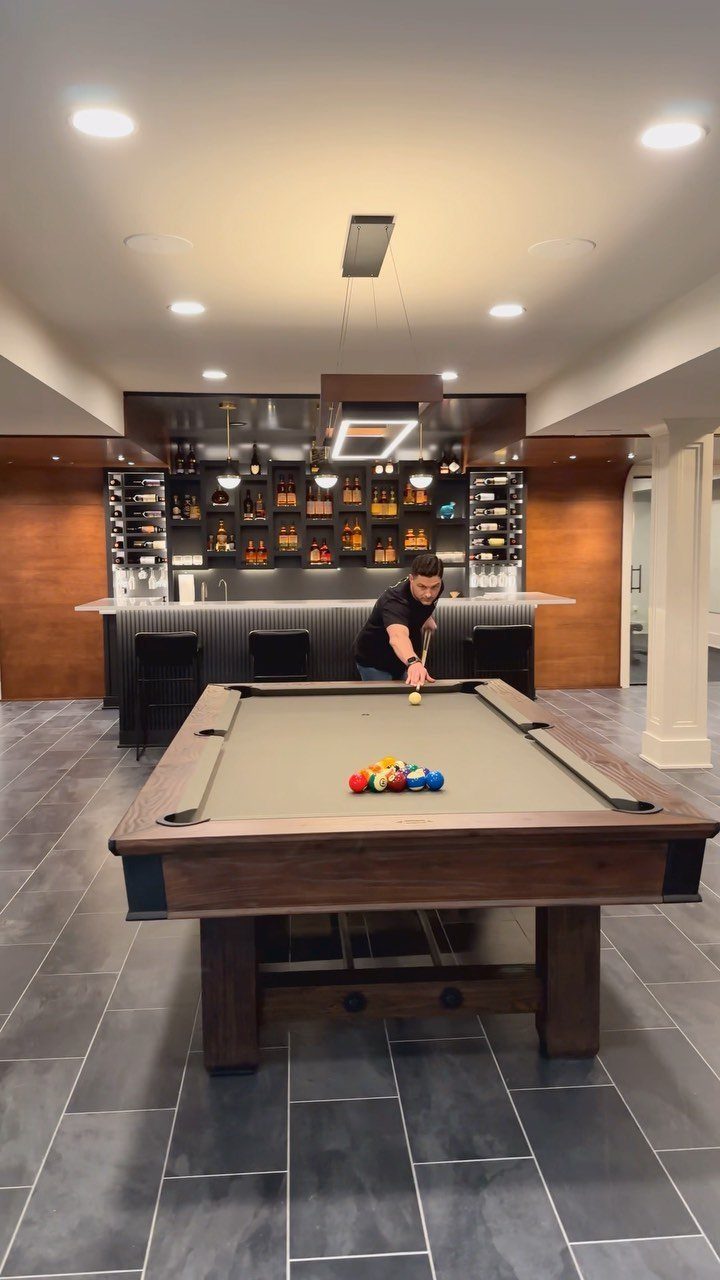 Pool table in a basement game room with a built-in bar in background
