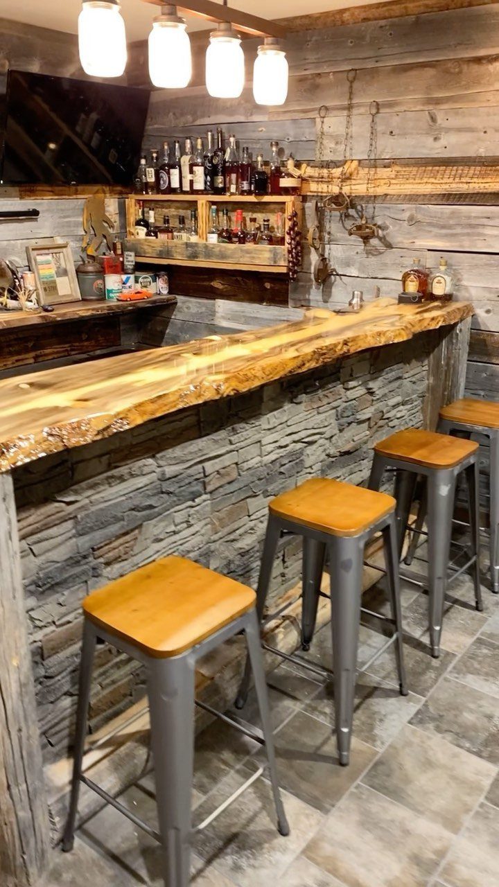 Rustic basement bar with live-edge wood counter, stone base, and metal bar stools.