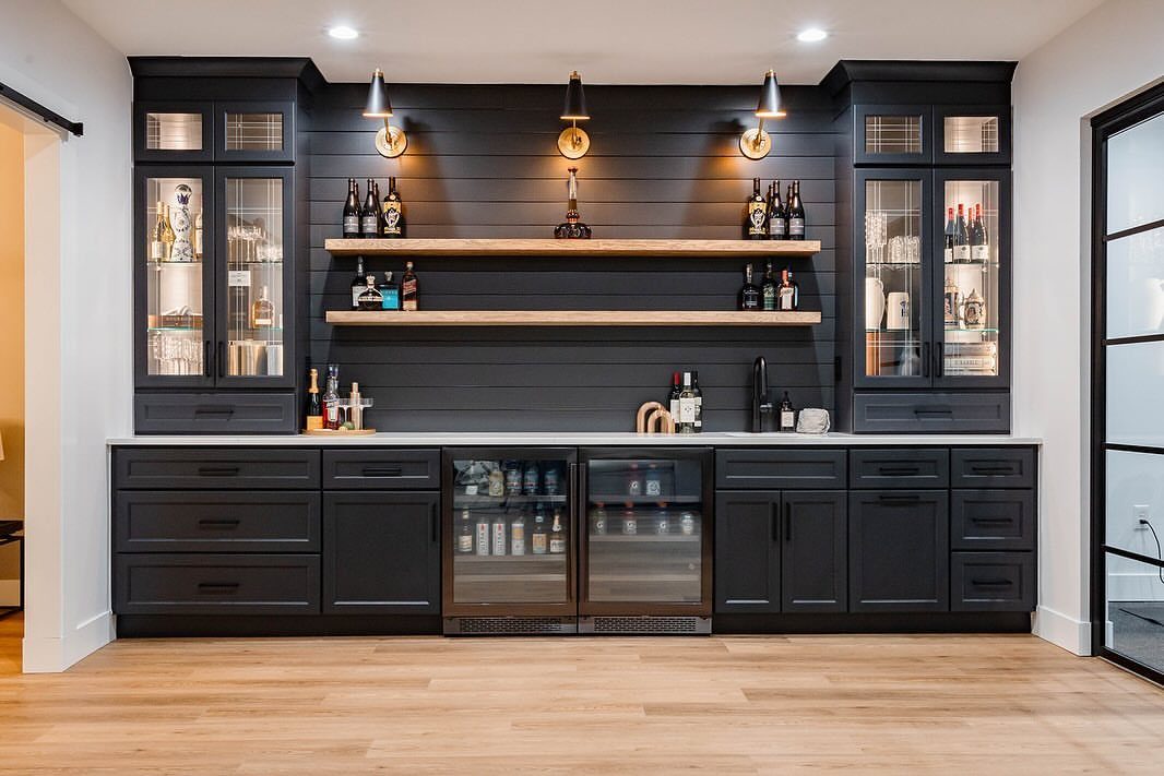 Modern home wet bar with dark grey cabinets, white counters, and gold lighting.