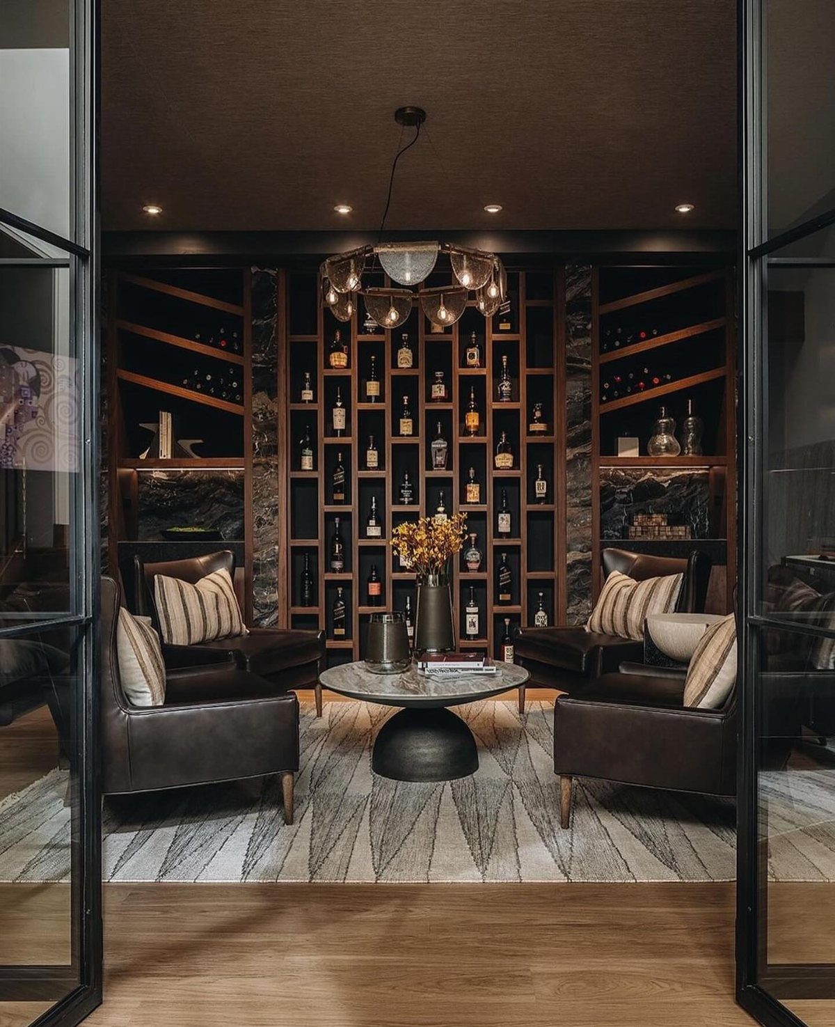 Dark lounge with leather chairs and a large wooden wall unit for wine and spirits.