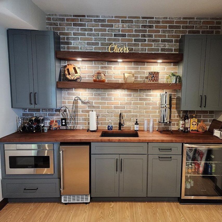 Basement bar with grey cabinets, wooden counters, and a stainless steel mini fridge.