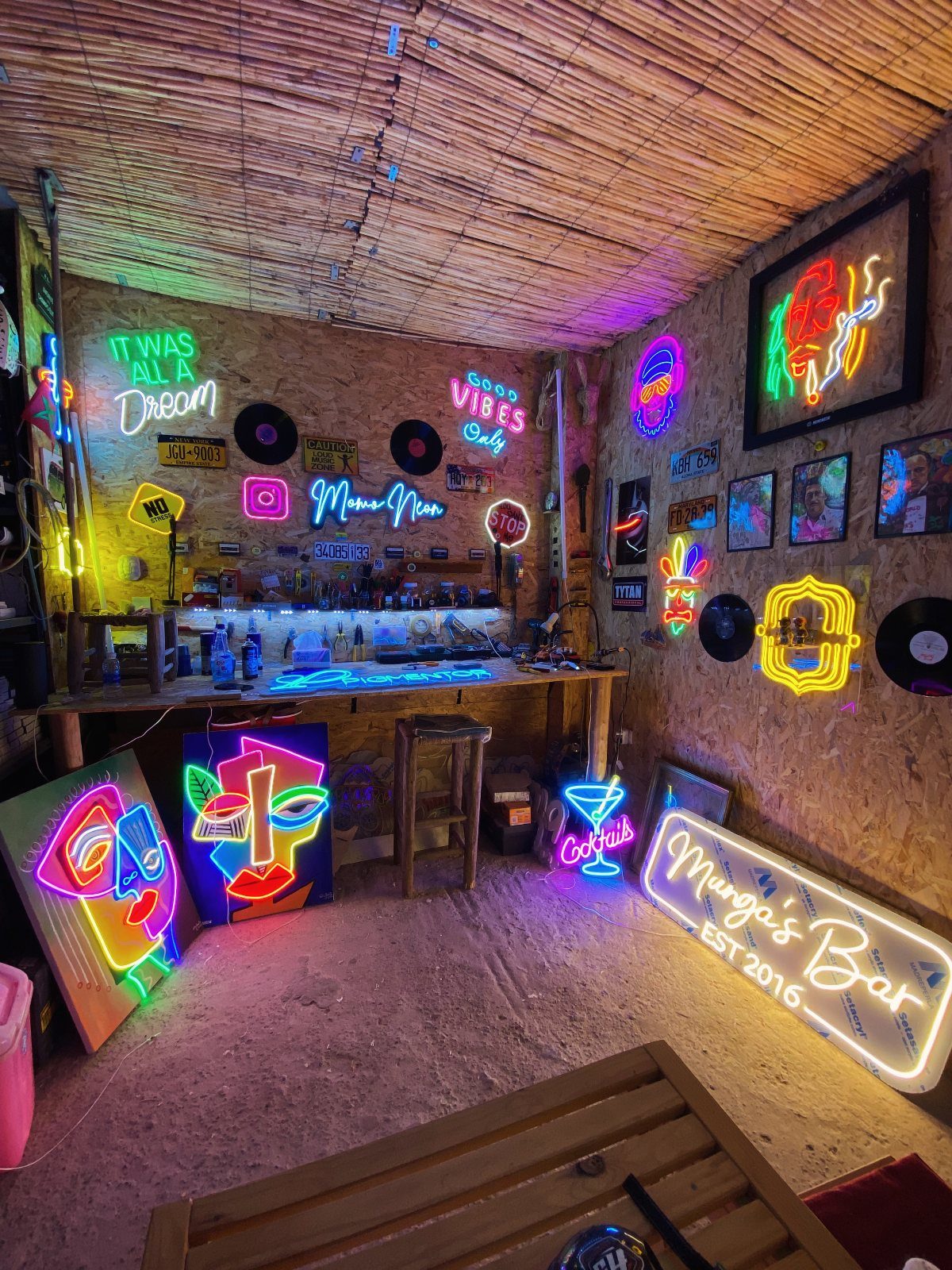 Rustic bar interior decorated with multiple colorful neon signs and bamboo walls.