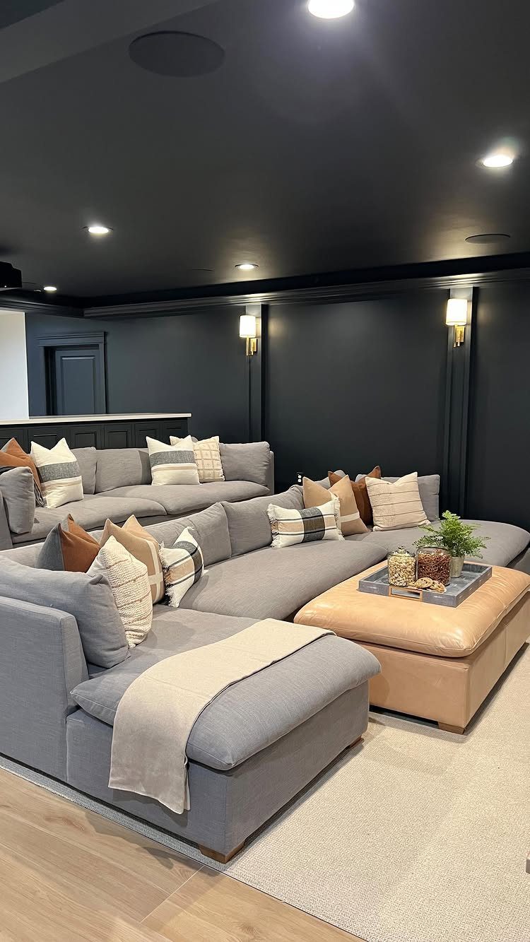 Large grey sectional sofa with neutral pillows in a dark modern basement lounge.