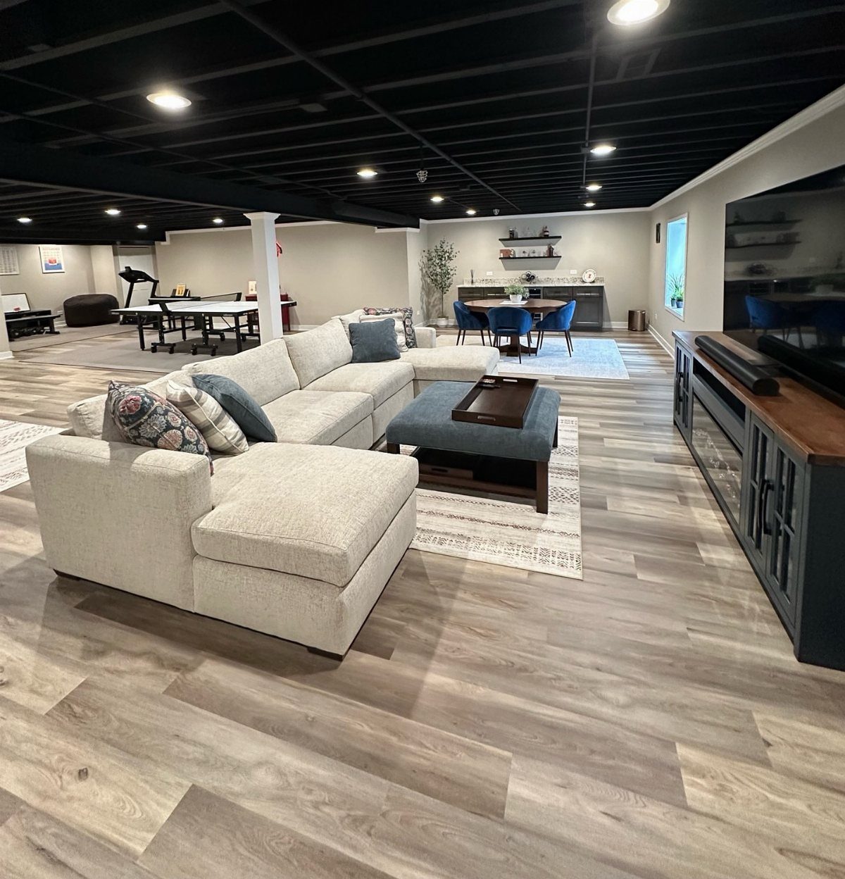 Finished basement man cave with sectional sofa, game table, and open layout design.