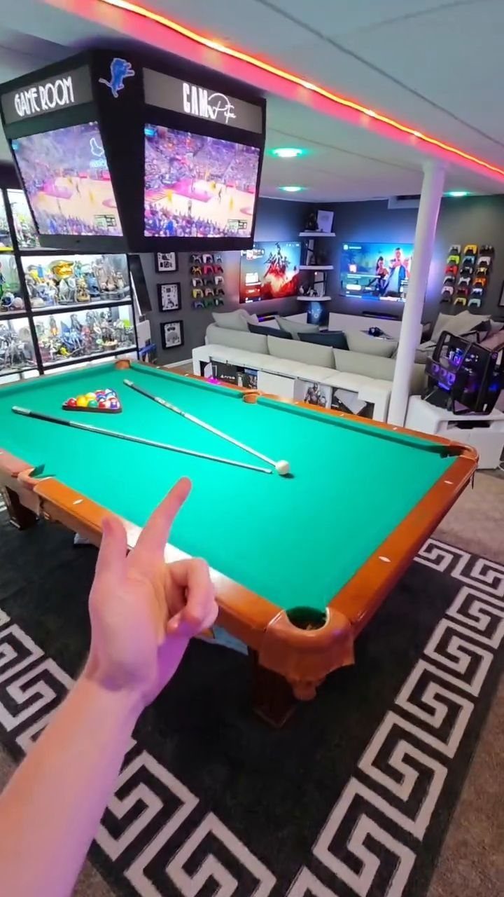 Green felt pool table in a modern basement game room with neon lighting.