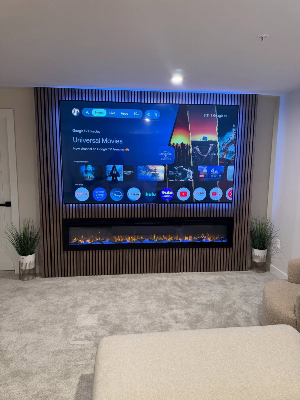 Large television and linear electric fireplace mounted on a brown slatted wood wall.