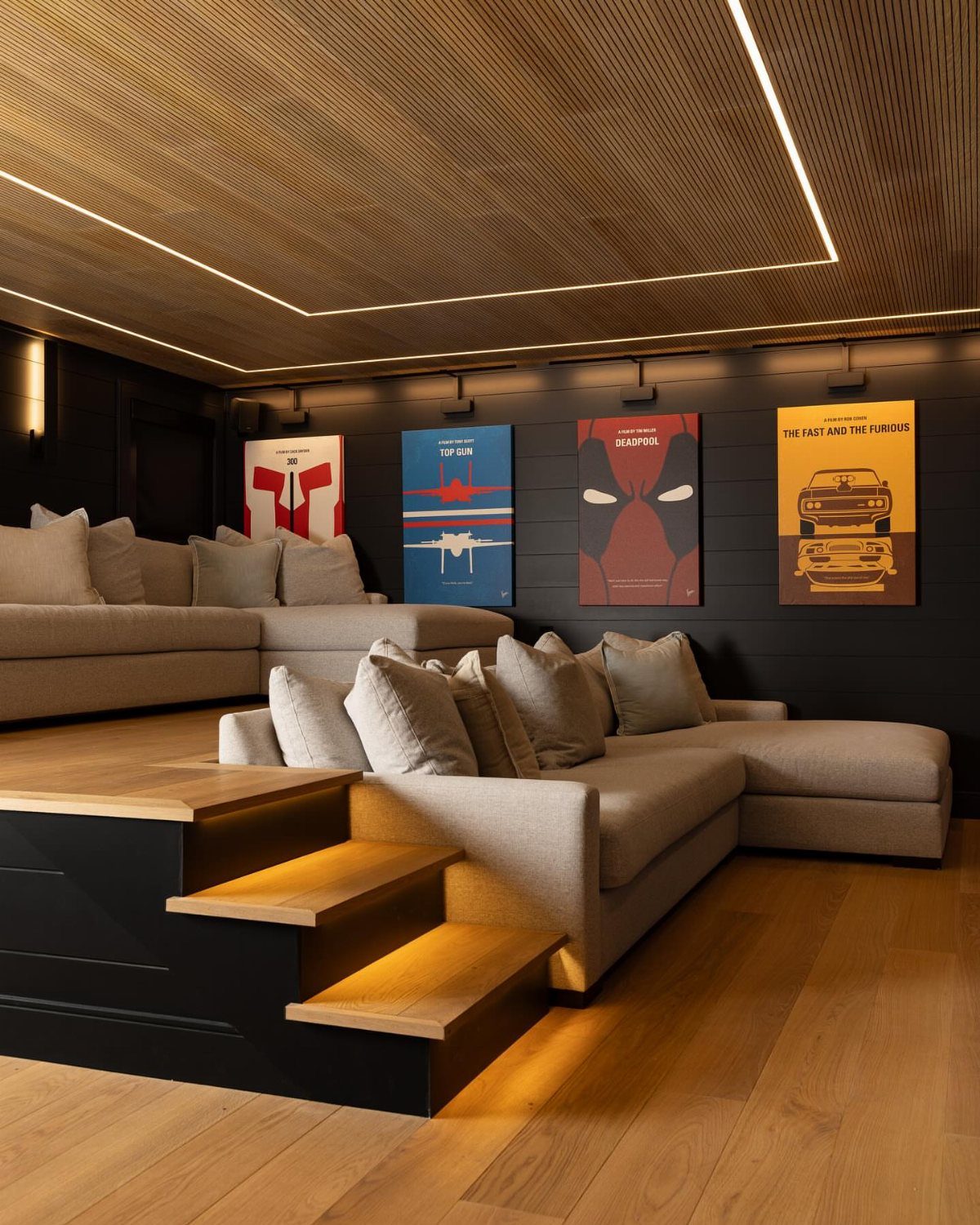 Tiered grey sectional sofas in a home theater with wooden accents and posters.
