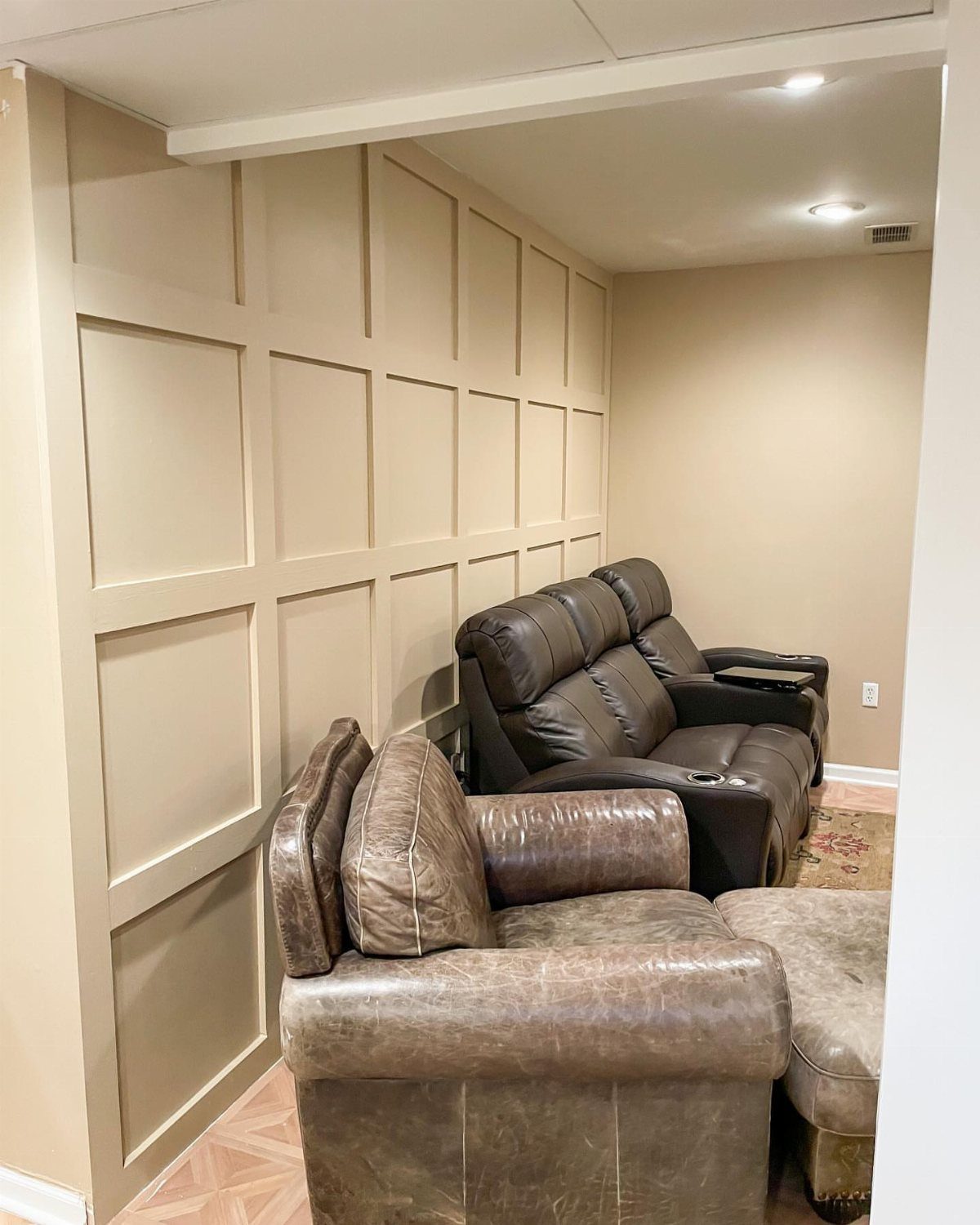 Brown leather reclining sofas in a basement room with beige paneled walls.