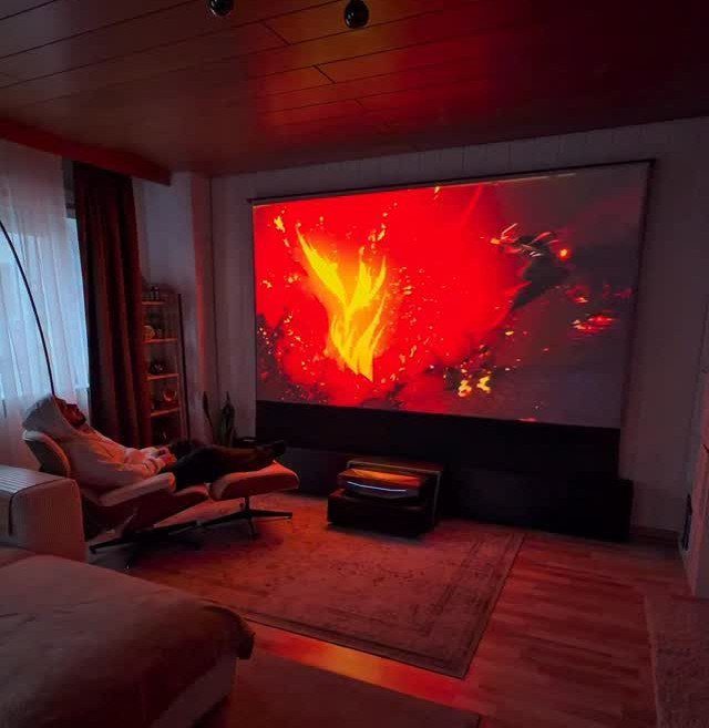 Large projection screen showing fire in a home theater with lounge seating.