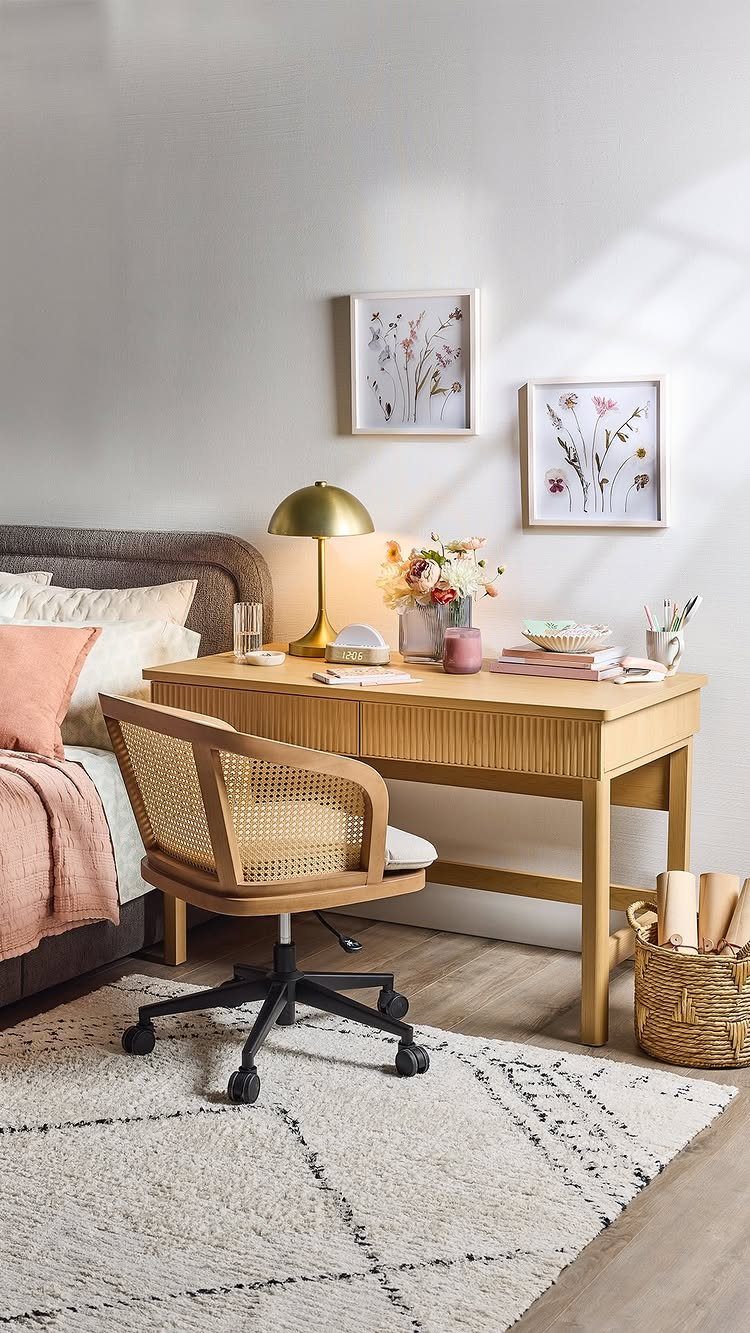 Light wood desk used as a nightstand next to a bed with pink linens.