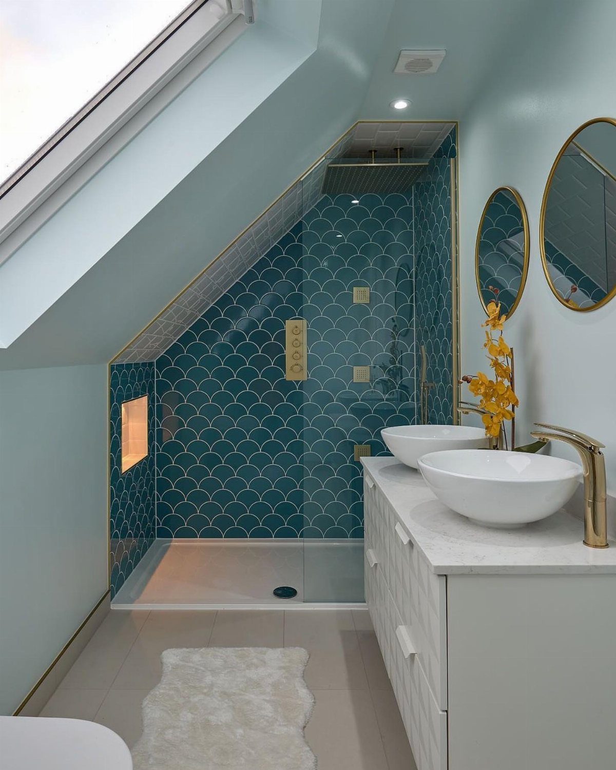 Attic bathroom with teal fish-scale shower tiles, white vanity, and sloped blue ceiling.