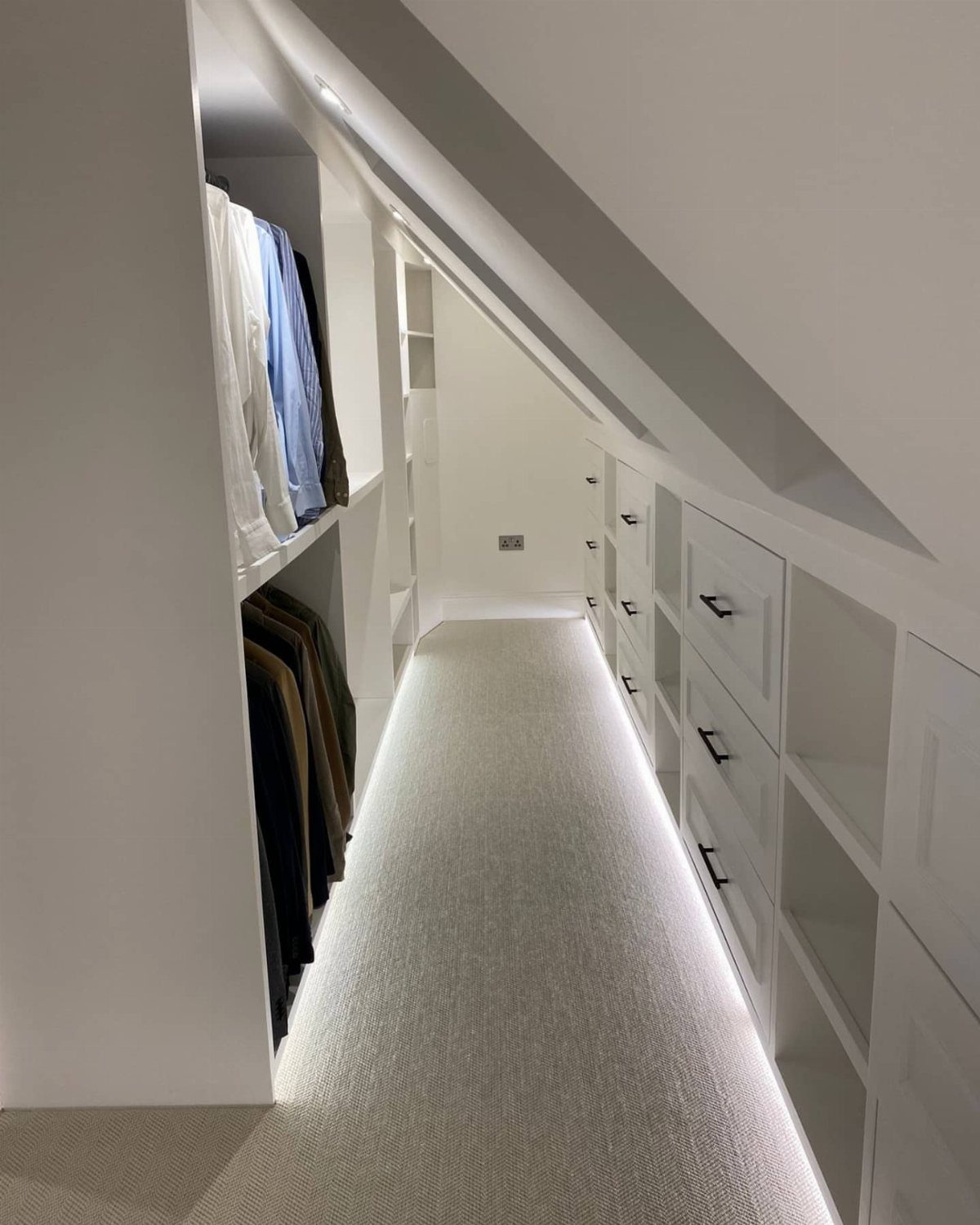 White attic walk-in closet with sloped ceilings, built-in drawers, and integrated LED lighting.