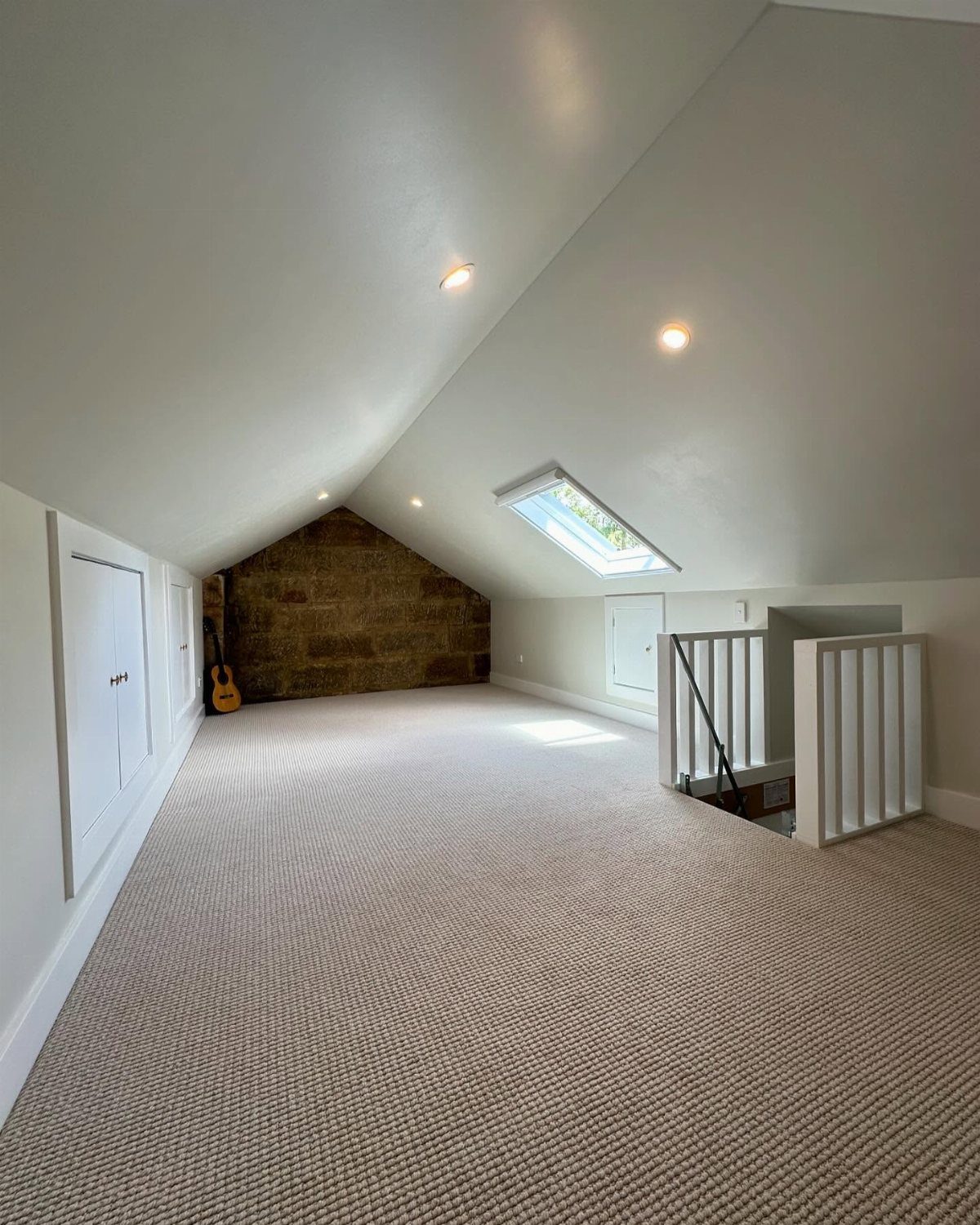 Empty attic room with white sloped ceilings, beige carpet, and a ceiling skylight.