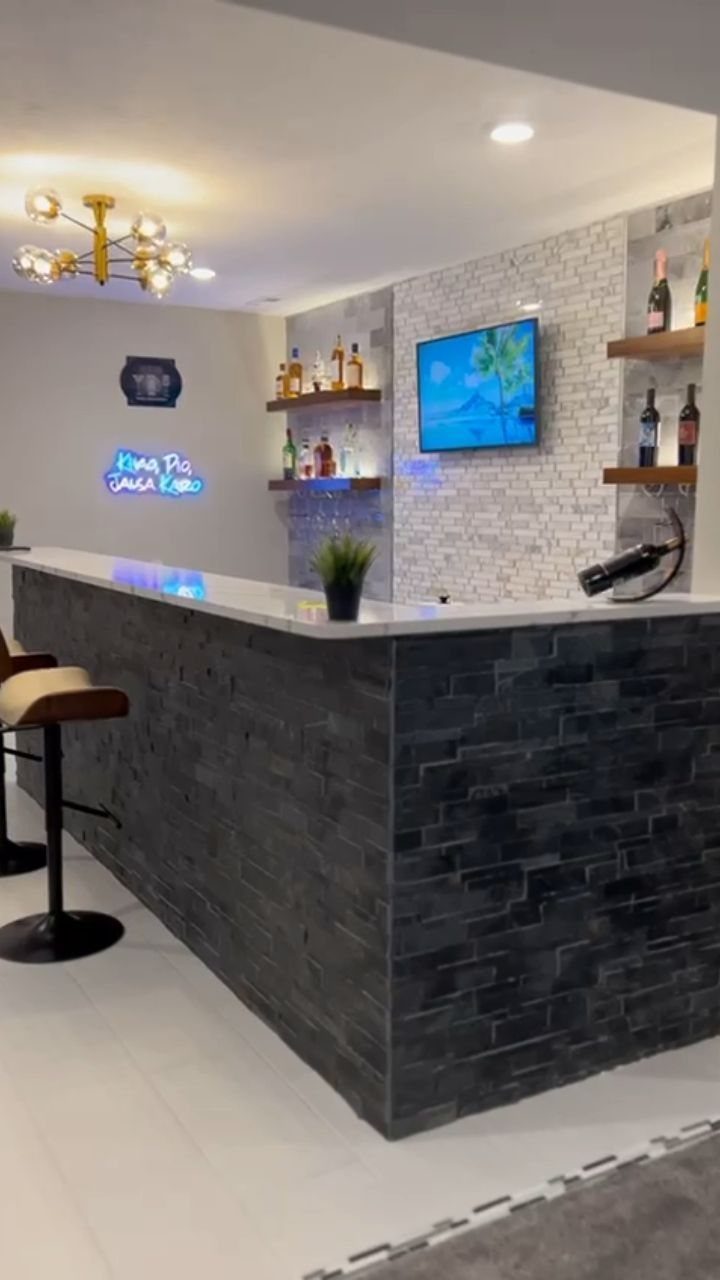 Modern home bar with dark stone base, white countertop, and floating bottle shelves.
