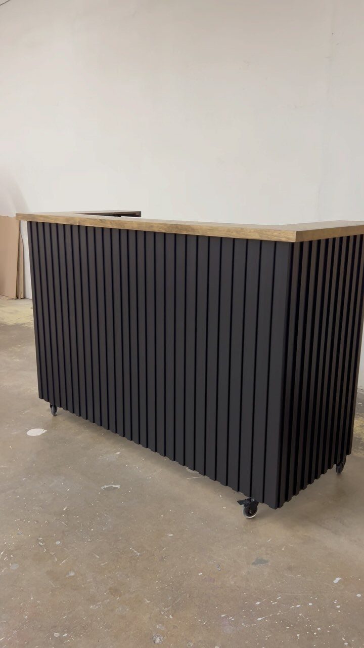 Portable bar with a light wood top and black slatted wooden base on wheels.
