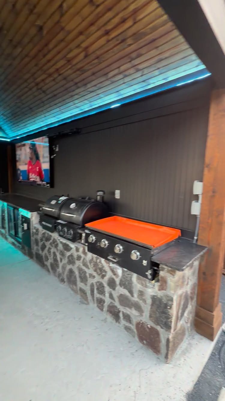 Outdoor bar with stone base, built-in grill, and blue LED ceiling lighting.