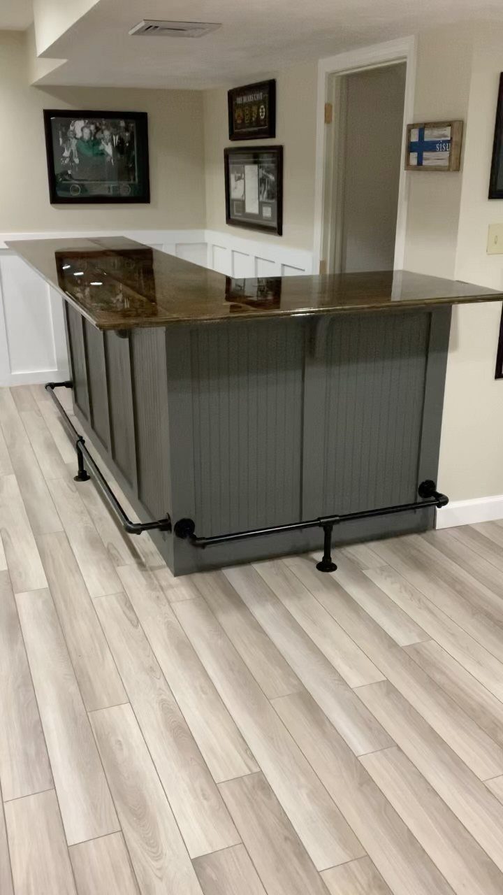 Polished brown granite countertop on a grey home bar with black foot rail.