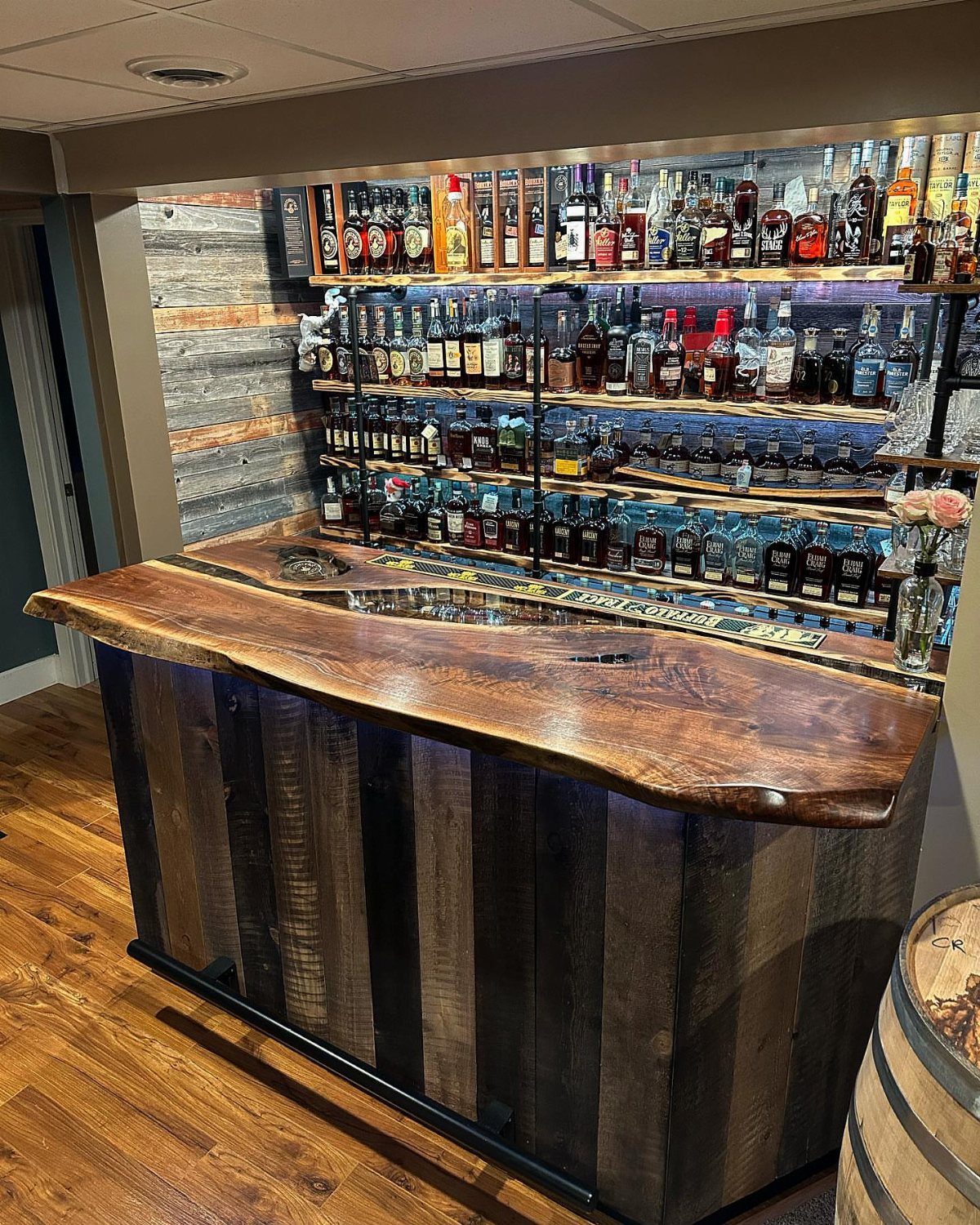 Home bar with live-edge wood countertop and shelves stocked with liquor bottles.