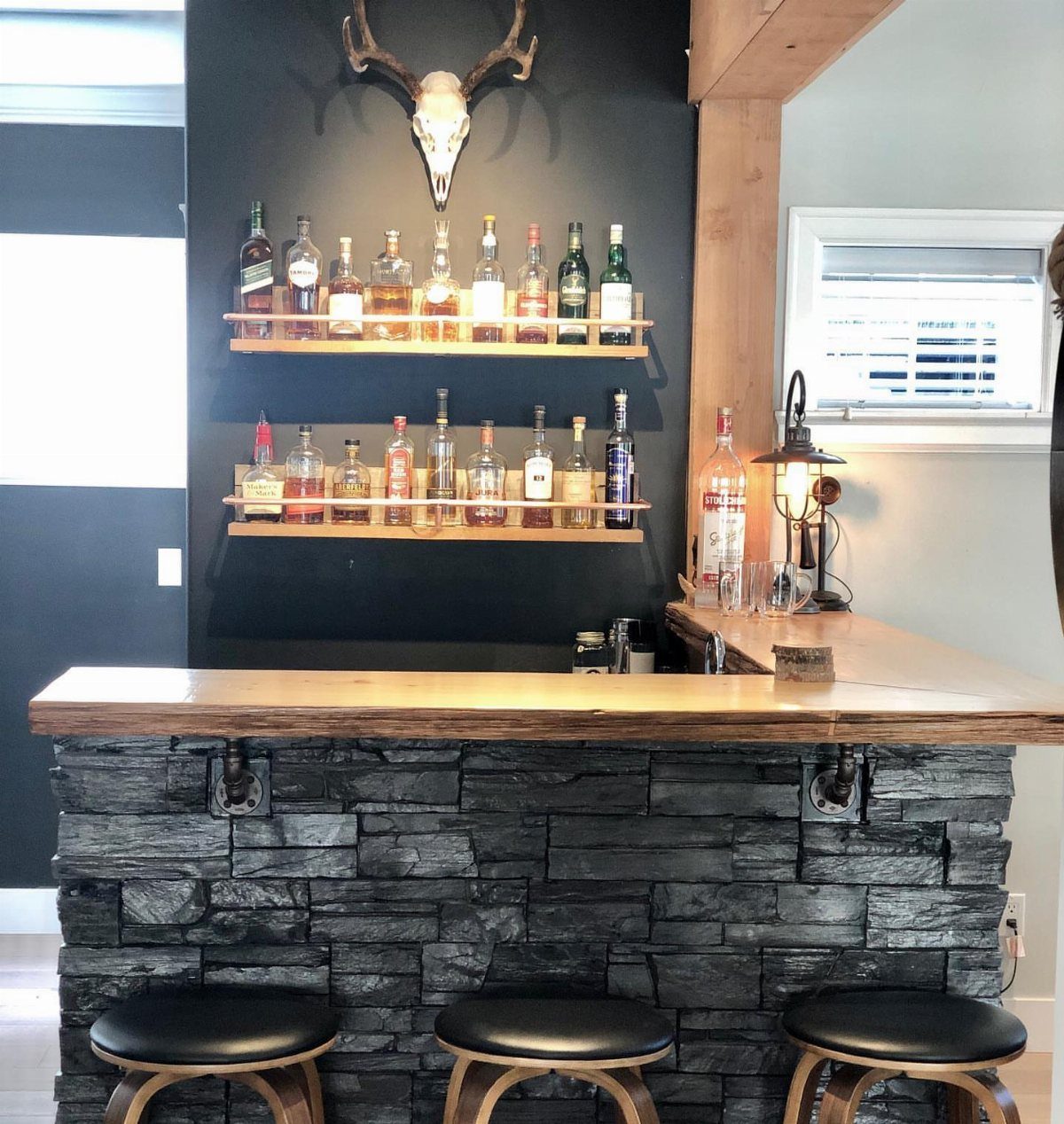 Home bar with wooden countertop, stone base, and liquor bottles on shelves